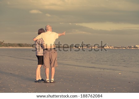 A married couple in retirement on the beach at sunset in Florida pointing at something on the horizon.