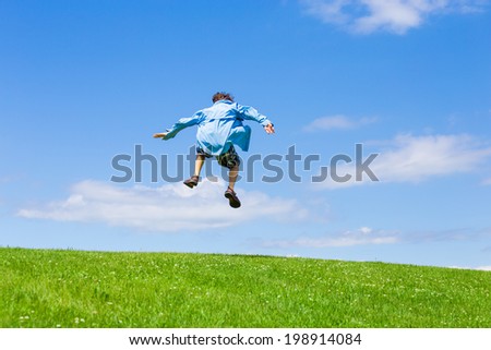 Back view of a teen boy jumping in the air on a sunny summer day.