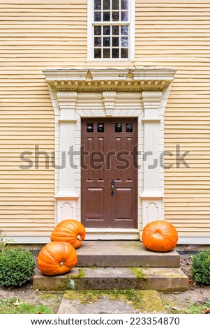 An old Colonial era antique front door to a period wooden clapboard home with pumpkins.