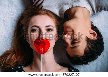 Loving couple lying on the floor girl covers her mouth with a lollipop