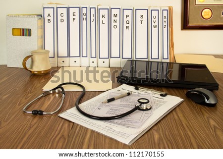 Notebooks, files, laptop, prescriptions, coffee cup and stethoscope fill the desktop of a doctor.
