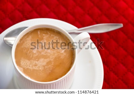 A cup of coffee with swirled milk in a white cup and saucer sits on a red mat.