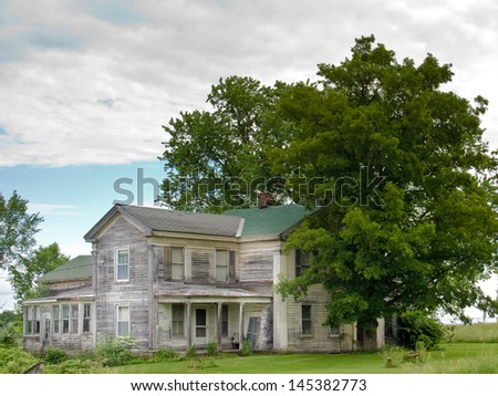 Under gray, cloudy skies, a ramshackle  gray house sits in the countryside in Schenectady county, NY.