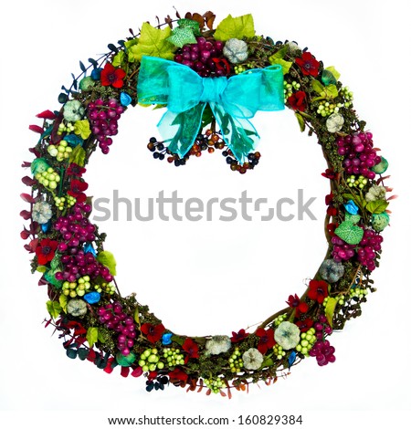 The decorations on a grapevine wreath are the colors of burgundy, green, blue-green, and dark blue and feature grapes, seed pods, husks, leaves, berries, flowers and eucalyptus with a blue-green bow.