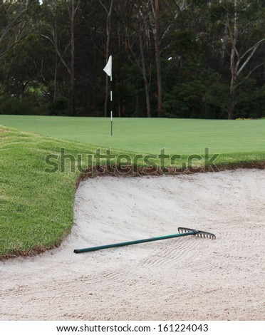 Golf course sand bunker with rake and flag in background