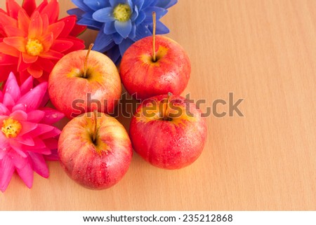Ripe four red apple with artificial flower on plywood background