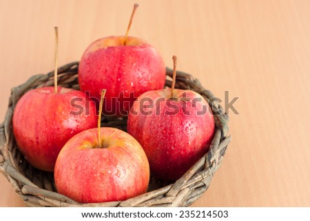 Ripe four red apple in the basket on plywood background