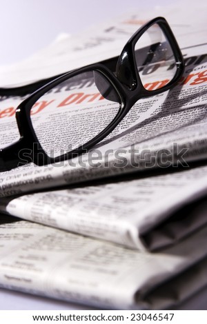 A black frame eyeglasses on a stack of newspaper.