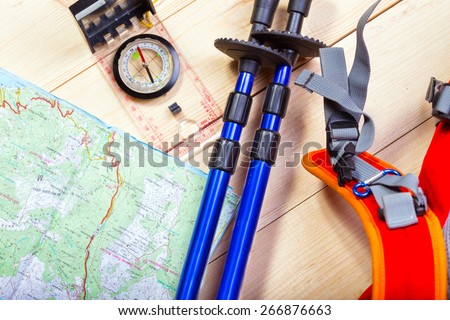 compass, map, trekking poles and backpack on a wooden background