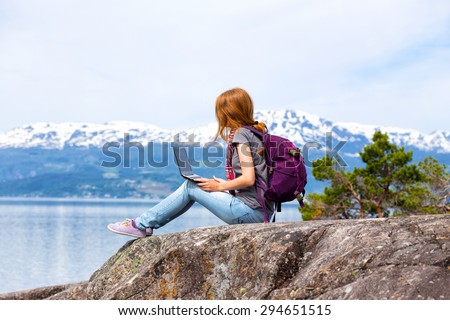 girl hikerl with a laptop sitting on a rock on a background of mountains and lakes