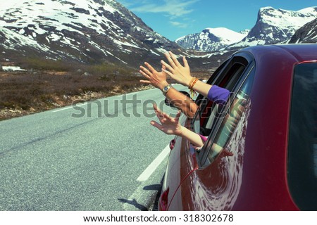 hands of men and children peering out of the car on a background of mountains