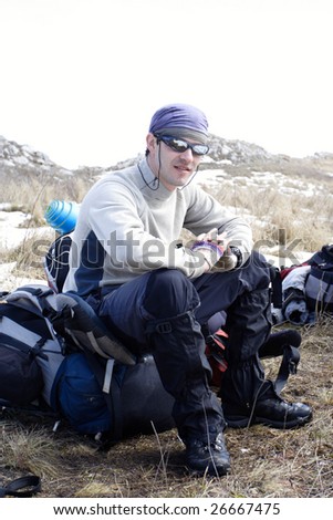smiling young hiker in glasses sitting on a backpack