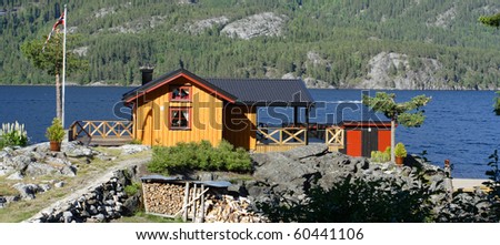 traditional norwegian wooden house standing at the lakeside and mountains in the distance