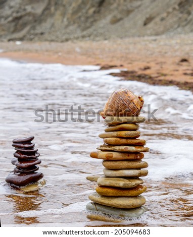 Pyramid of round stones and shell in the calm sea water at the beach. Soft warm light, time before sunset