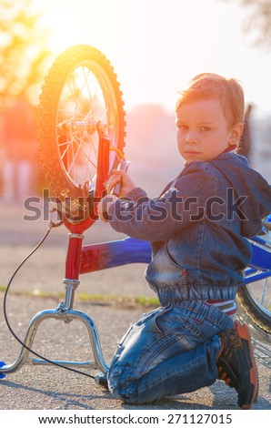 Little boy is pumped European wheel of his bike, sitting on the pavement against a bright setting sun. natural composition