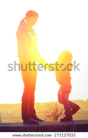 Young mother and son holding hands and laughing standing on the parapet on the background of the backlight. Family Vintage composition