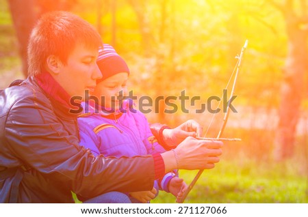 Dad teaches his son to shoot a bow, which they did together against the bright sun in the park. family composition
