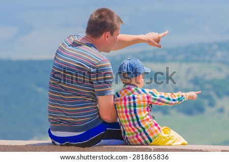 Small son and dad show each other something in the distance. Family composition