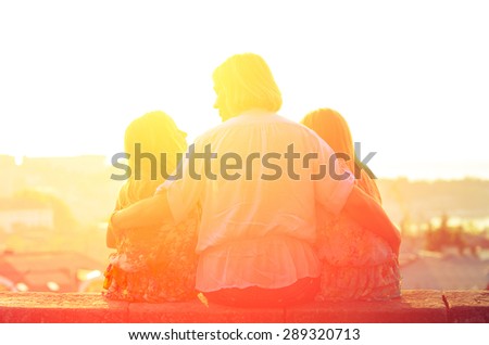 Mom and two sisters twins sitting on the parapet and watch the sunset. Family vintage composition