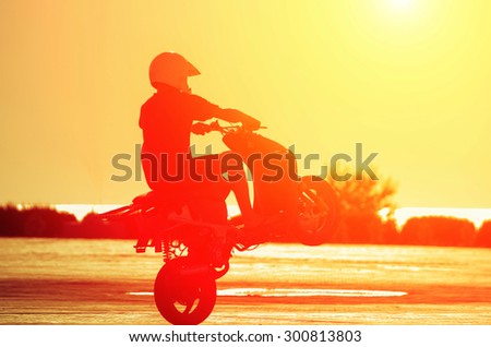 A man in a helmet on a moped shows stunts at sunset. Natural composition