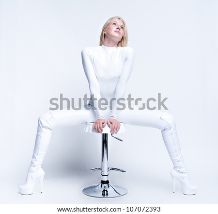 Young female contortionist in glossy vinyl suit sitting on a bar chair