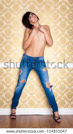 Pretty brunette wearing blue jeans and heels posing on a gold wall