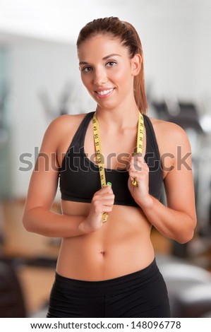Fit woman holding a measuring tape around her neck in a gym