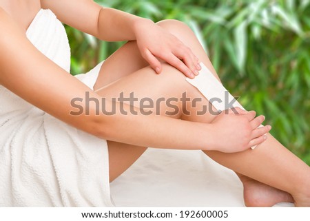 Woman removing hair from her legs with wax, in a green background