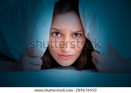 Woman with a pillow over her head, not wanting to get out of the bed in the dark