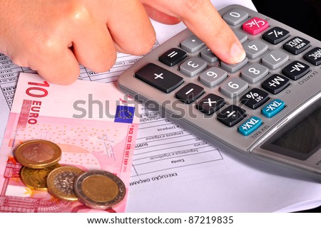 Business person doing accounts using a calculator with some money on the side