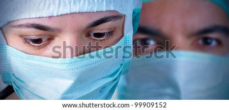 Closeup portrait of two surgeons during a surgery. Blue cast and vignetting applied.