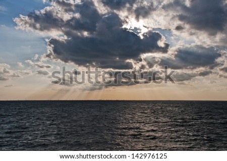 Sunset over large body of water with rays of light coming through clouds