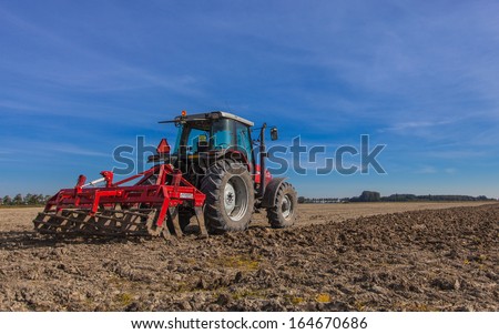 Farming in the Netherlands Tractor with Plough Plowing in a Field under Blue Sky Farming in the Netherlands Tractor with Plough Plowing in a Field under Blue Sky