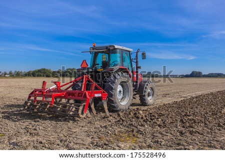 Farming In The Netherlands, Tractor With Plough In A Field Under Blue Sky