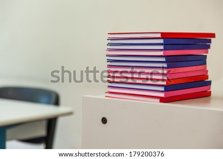 Stack of Multicolored Notebooks on a Drawer with School Furniture in Background