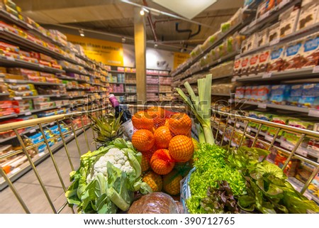 Grocery trolley cart at a supermarket aisle filled up with healthy food products seen from the customers point of view