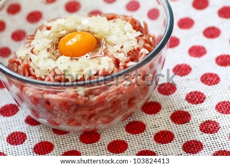Raw pork mincemeat with egg and chopped onion in a clear glass  bowl