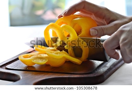 Female hands slicing yellow sweet pepper on chopping board