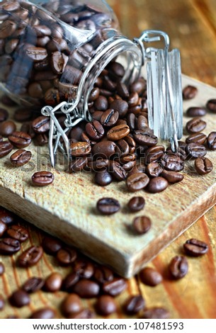 Close up of scattered roasted coffee beans from a clear glass jar on a wooden board