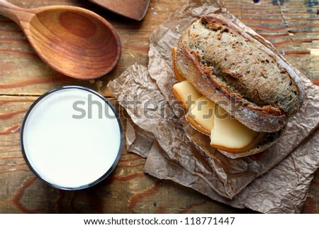 Top view on cut in halves whole grain bread roll with smoked cheese and a glass of milk