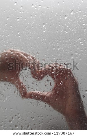 Female Caucasian hands in shape of heart behind wet glass