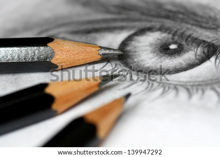Close up of graphite drawing pencils laying on paper with eye