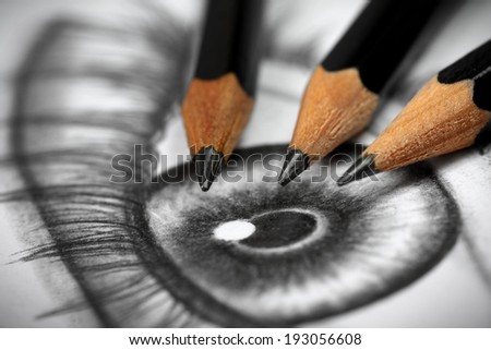 Close up of an eye drawing and three graphite pencils