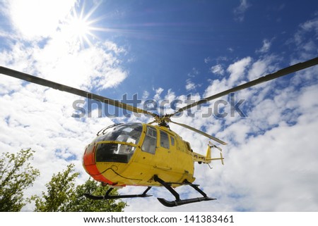 Yellow medical rescue helicopter flying above trees