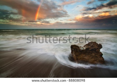 Sunset at the beach with rushing water and a rainbow