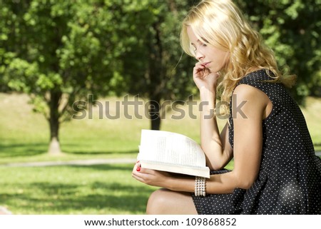 Young attractive blonde woman reading a book in park outdoor