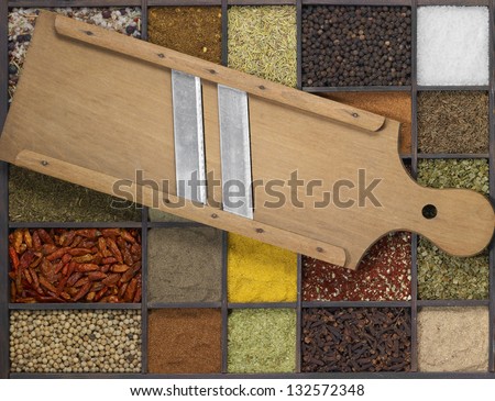 lots of various different spices in a framed dark wooden box with a old wooden mandolin slicer on it, seen from above