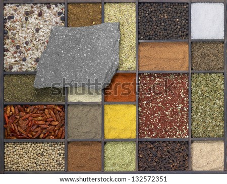 lots of various different spices in a framed dark wooden box with a flat stone on it, seen from above