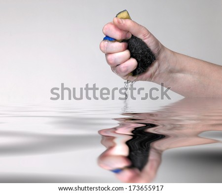 a hand pressing a wet sponge with dripping water over mirroring water surface