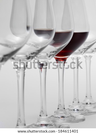 some wine glasses standing consecutive in a row in light grey back, one partly filled with red wine